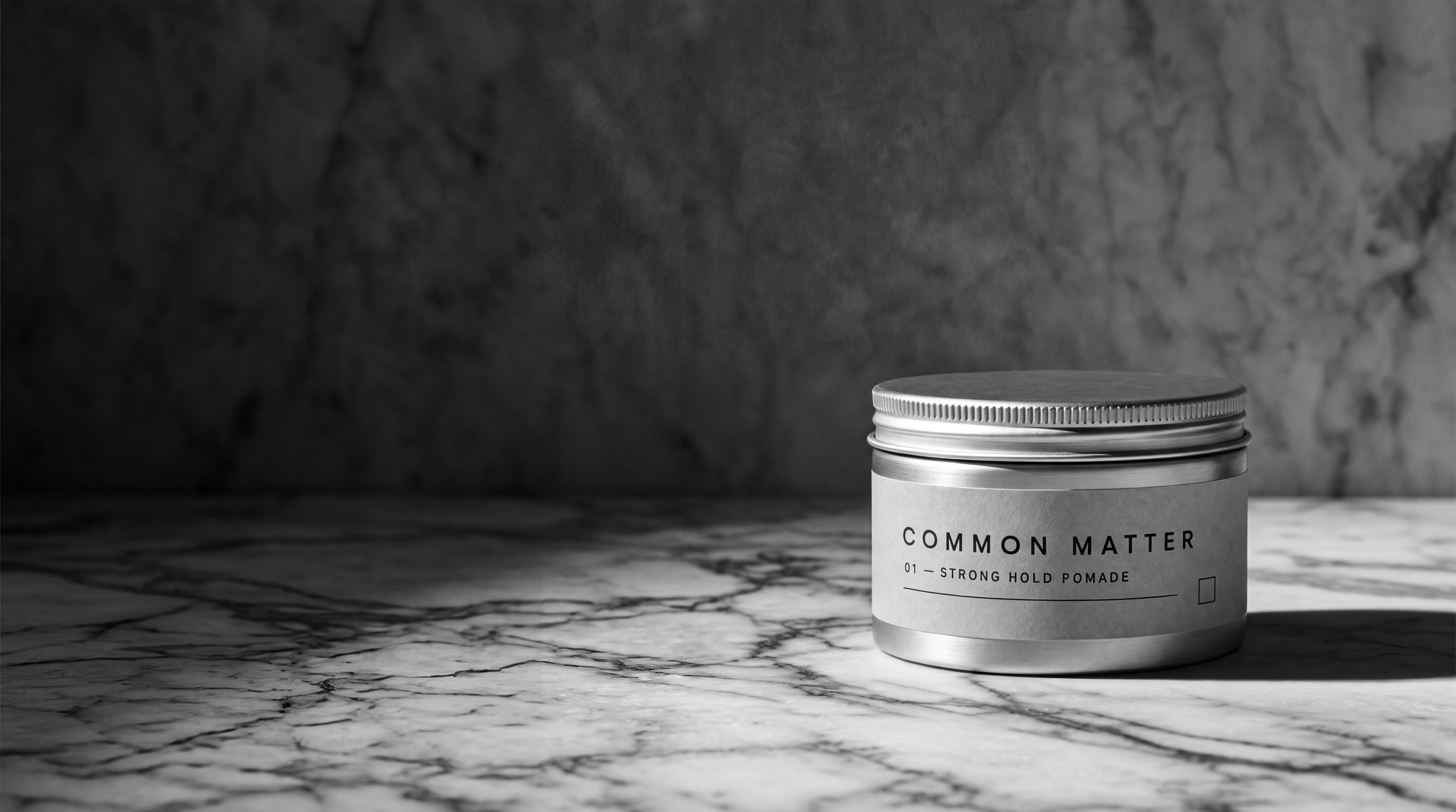 Common Matter No. 01 pomade tin on marble under hard light